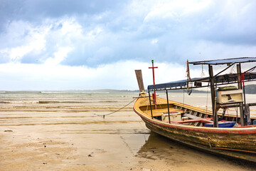 A lone traditional fishing boat rests on the sandy shore under a cloudy sky, coastal activities and the tranquility of maritime environments. Copy space