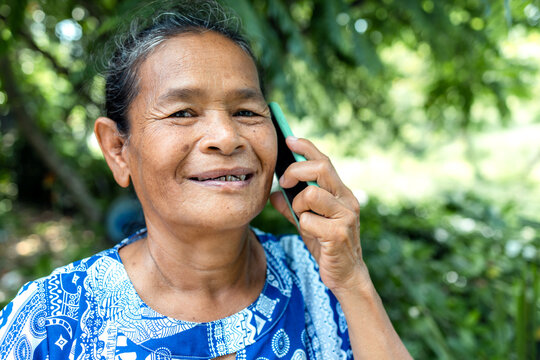 happy asian senior mature woman relaxing in garden, speaking on mobile phone with family, thai asia elderly grandmother enjoy smart outdoor lifestyle with wireless technology and digital device