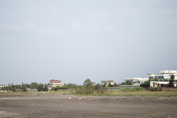 Fototapeta premium Distant view of a coastal neighborhood with modern villas arranged along a low shore. A large pale sky occupies much of the frame, placing the houses as a thin band above the empty foreground