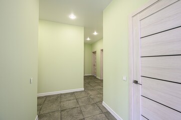 pale green hallway features dark tile flooring, recessed lighting, and light-colored doors with horizontal accents. The walls are smooth and simple