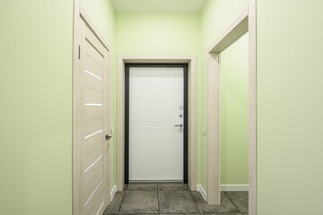 bright hallway featuring a white front door with a black frame, flanked by two light-colored wooden doors against light green walls