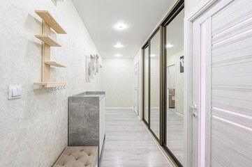 Bright hallway with light walls, wooden floors, a mirrored wardrobe, and a wooden shelf. Modern design