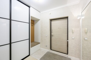 bright entryway features a white wardrobe with black trim, a built-in bench, a light wood door with dark trim, and a mirror, creating a modern and organized space