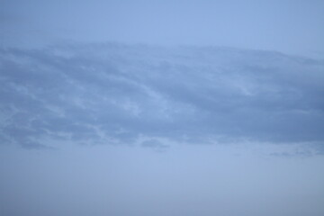 Obraz premium Calm evening sky with a long smooth cloud bank drifting across a pale blue background, photographed without ground elements to emphasize the atmospheric form. Soft illumination creates delicate