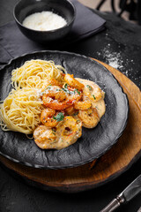 Pasta with shrimps in creamy sauce in a plate on black background vertical photo