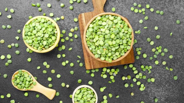 Dried green split peas are arranged in natural wooden bowls and scattered on a dark textured surface, perfect for healthy vegan recipes. 