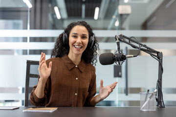 Woman host recording a podcast session in a modern studio setup with professional equipment, expressing enthusiasm and confidence.