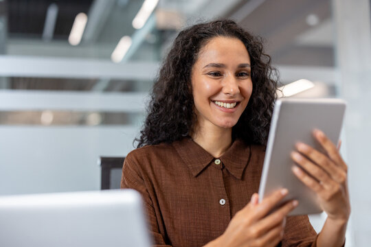 A cheerful woman interacts with a tablet in a bright, professional workspace. The contemporary setting and her smile convey positivity, connection, and productivity - Powered by Adobe