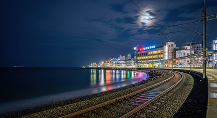 Fototapeta premium Nighttime coastal train station with vibrant city lights reflecting on the water