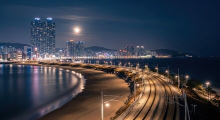 Night cityscape panorama of a coastal city, featuring a beach, illuminated train tracks, and skyscrapers under a full moon
