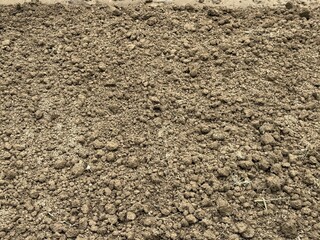 Brown earthy texture shows rich tilled soil scattered lightly with pieces of grass and sand