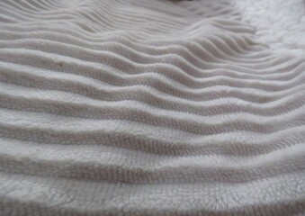 A macro perspective transforms the soft, wavy ridges of a white blanket into an abstract pattern. 