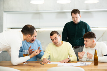 Male friends read a financial or legal document, drink beer and try to solve financial problems by consulting each other while sitting at the table