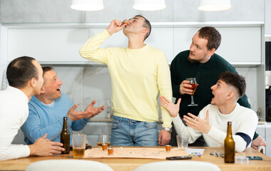 Friends drinking beer and enthusiastically playing a board game at home
