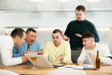 Group of male friends solving problems using laptop and drinking beer at home