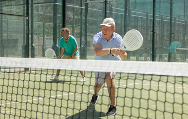 Mature sporty man playing padel game in court on sunny day