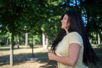 Fototapeta premium Beautiful smiling fit woman running in park on sunny morning, side view of healthy outdoor fitness activity