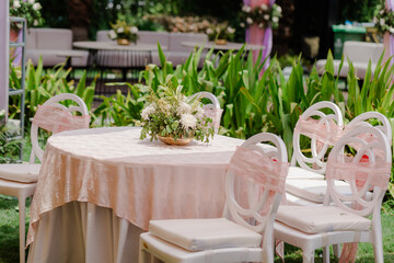 Outdoor event setup with round tables and white chairs adorned with pink ribbons. Elegant floral centerpieces add a touch of nature's beauty.
