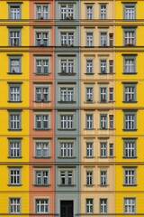 Naklejka premium Pattern of windows on a colorful European apartment building facade with repeating yellow and green sections and ornate architectural details