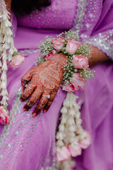 Intricate henna design on a hand adorned with a floral corsage and rings, resting on a shimmering...