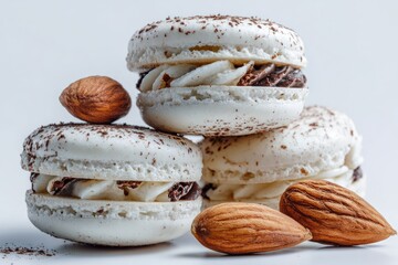 Three delicate white macarons with creamy vanilla and chocolate filling, topped with cocoa powder, artfully arranged with three almonds on a white background