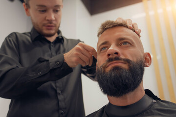 Obraz premium A skilled hairdresser is shaping a man's bald fade haircut and trimming his beard in a contemporary barbershop. The atmosphere is relaxed, focused on grooming and style