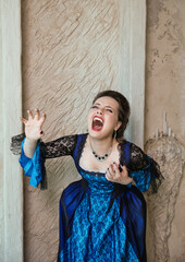Beautiful gothic vampire woman wearing medieval dress screams standing against ancient wall
