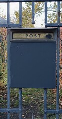 An antique mailbox on a gate leading into an autumn garden.