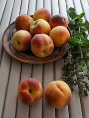 Still life with peaches in a clay bowl and mint branches.
