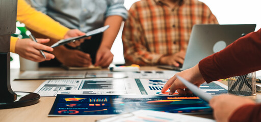 A diverse group of professionals collaborates in a modern office setting, analyzing data charts and graphs to develop effective business strategies through teamwork. SACTR