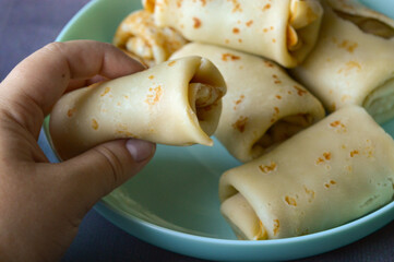 close-up hand holding rolled pancake crepe filled with sweet savory filling light blue plate homemade comfort food traditional cooking comfort food breakfast recipes family meals