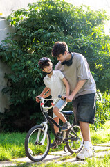 Obraz premium Older brother teaching younger child to ride bicycle in park with safety helmet. Big brother helping little child learn bicycle riding skills in sunny park. 