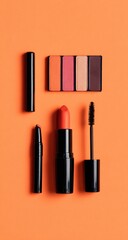 Flatlay of black cosmetic tubes, lipstick, eyeshadow palette, and mascara against a vibrant orange backdrop