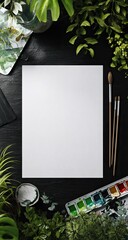 Blank white canvas surrounded by lush greenery, paintbrushes, and watercolor paints on a dark surface