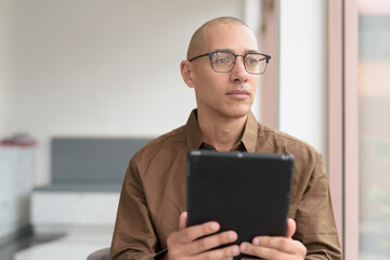 Confident bald Latin man using smartphone in coffee shop, casual tech-savvy lifestyle with glasses