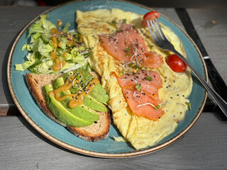 Delicious avocado toast topped with omelet and red fish, served on wholegrain bread. Healthy breakfast or brunch on a wooden table in natural light.




