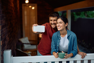 Happy couple taking selfie with cell phone on porch.