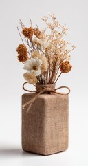 Dried floral arrangement in a beige, textured, square vase, tied with twine.  Neutral tones, minimalist aesthetic