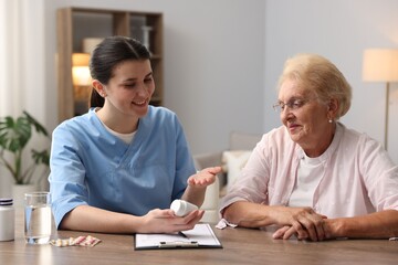 Nurse giving pills to senior woman at wooden table indoors. Home health care service