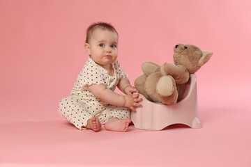 Cute little baby sitting near potty with toy bear on pink background