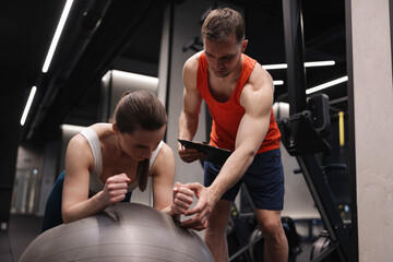 Fototapeta premium Young woman exercising with fitness ball near professional personal trainer in gym