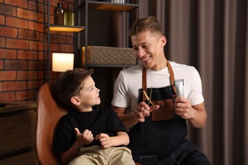 Professional barber with scissors, trimmer and little boy in barbershop