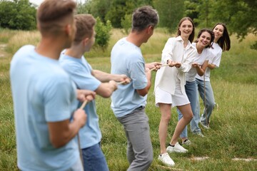 Fototapeta premium Team building. Group of happy people playing tug of war with rope outdoors