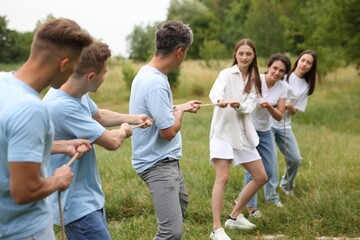 Team building. Group of happy people playing tug of war with rope outdoors