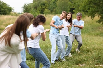 Fototapeta premium Team building. Group of happy people playing tug of war with rope outdoors