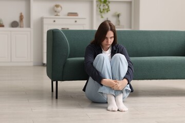 Sad young woman sitting on floor at home