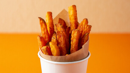 Crispy sweet potato fries served in a white paper cup against an orange background