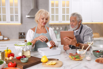 Elderly couple with tablet cooking together at marble table in kitchen
