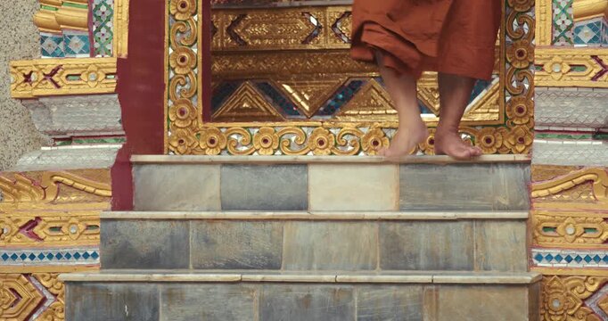Buddhist monks walks barefoot down the temple steps after completing the evening chanting ritual, surrounded by ornate Thai architecture.
