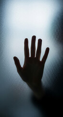 Silhouette of hand on frosted glass, conveying themes of isolation, mystery, or unseen presence.  Suggests a barrier or separation.